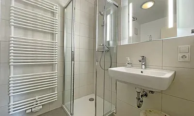 Badezimmer mit Dusche, WC, Kosmetikspiegel, Waschtisch und einem mobilen Wäscheständer