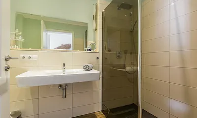 Badezimmer mit ebenerdiger Dusche, Waschbecken, WC, Kosmetikspiegel, beheizbarem Handtuchtrockner, Fön sowie leistungsfähiger Entlüftungsanlage