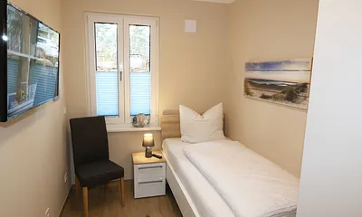 Schlafzimmer mit einem Einzelbett (0,90 m x 2,00 m), Nachttischablage, Kleiderablage, Kleiderschrank und einen weiteren Smart-TV