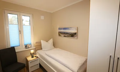 Schlafzimmer mit einem Einzelbett (0,90 m x 2,00 m), Nachttischablage, Kleiderablage, Kleiderschrank und einen weiteren Smart-TV