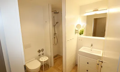 Badezimmer mit ebenerdiger Regendusche, Waschtisch, WC, Fön, Kosmetikspiegel und einem Handtuchtrockner  