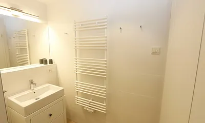 Badezimmer mit ebenerdiger Regendusche, Waschtisch, WC, Fön, Kosmetikspiegel und einem Handtuchtrockner  