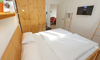 Schlafzimmer mit Doppelbett (1,80 m x 2.00 m), verstellbare Lattenroste, Nachttischablagen, Ganzkörperspiegel, Kleiderablage, geräumiger Kleiderschrank, Smart-TV sowie Verdunklungs-Vorhängen