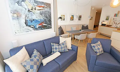 gemütlicher Wohn-/ Essbereich mit hellen Eichenholz Möbeln, Sessel, Couch mit Leselampe, Beistelltische, Stehlampe & 65“ Smart-TV 