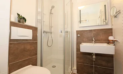 Badezimmer mit ebenerdiger Dusche, Waschplatz, WC, Handtuchheizkörper, Kosmetikspiegel und Fön