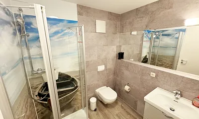 innenliegendes Badezimmer mit WC, Dusche, Waschtisch mit Unterschrank, Fön, Kosmetikspiegel, großem Wandspiegel, Handtuchheizkörper und einem Ablageregal