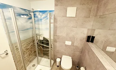 innenliegendes Badezimmer mit WC, Dusche, Waschtisch mit Unterschrank, Fön, Kosmetikspiegel, großem Wandspiegel, Handtuchheizkörper und einem Ablageregal