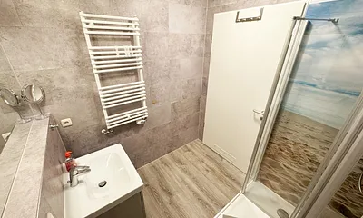 innenliegendes Badezimmer mit WC, Dusche, Waschtisch mit Unterschrank, Fön, Kosmetikspiegel, großem Wandspiegel, Handtuchheizkörper und einem Ablageregal