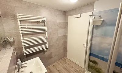 innenliegendes Badezimmer mit WC, Dusche, Waschtisch mit Unterschrank, Fön, Kosmetikspiegel, großem Wandspiegel, Handtuchheizkörper und einem Ablageregal