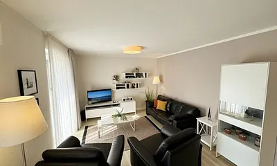 Wohnbereich mit modernen weißen Hülsta Möbeln, ein gemütliches Ledersofa, zwei Sessel, zwei Couchtischen, Stehlampen, DAB Radio mit CD-Player und Bluetooth, Smart-TV mit Soundbar & Blu-Ray Player