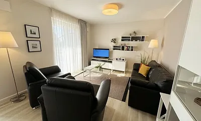 Wohnbereich mit modernen weißen Hülsta Möbeln, ein gemütliches Ledersofa, zwei Sessel, zwei Couchtischen, Stehlampen, DAB Radio mit CD-Player und Bluetooth, Smart-TV mit Soundbar & Blu-Ray Player