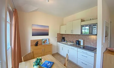 angrenzende Küchenzeile mit Keramikspüle, 3-Zonen-Glaskeramik-Kochfeld, Kühlschrank mit Gefrierfach, Geschirrspüler, Mikrowellen-Dunstabzugs-Kombination, Kaffeemaschine, Wasserkocher und Toaster