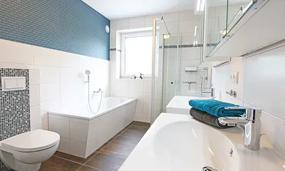 Tageslichtbad mit Badewanne, bodengleicher Echtglasdusche, 2 Waschtische mit Unterschränken und Spiegelschrank, WC, Kosmetikspiegel, Handtuchtrockner, Haarfön