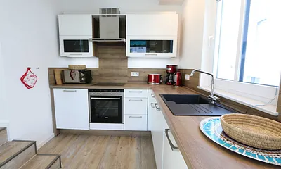 Küchenzeile mit Ceranfeld, Backofen, Geschirrspüler, Mikrowelle, Kühlschrank mit Gefrierfach, Kaffeemaschine, Wasserkocher, Toaster und diversen Küchenutensilien