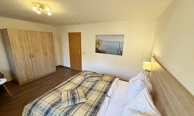 Schlafzimmer hell und modern eingerichtet mit Doppelbett, Komfortmatratzen (2x 0,90 m x 2,00 m), Nachttischkonsolen, Kleiderschrank und Verdunklungsgardinen