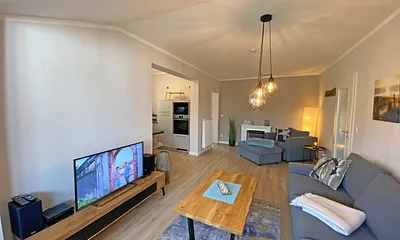 Wohnzimmer mit gemütlicher Couch, Couchtisch, Leselampe, Sessel, Hocker, Lowboard, Smart-TV, Blu-Ray Player, Teufel-Musikanlage mit Radio, DAB Radio, CD-Spieler, USB-Anschluss und Bluetooth