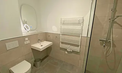 innenliegendes Bad mit einem Waschtisch, beheiztem und beleuchtetem Spiegel, Handtuchheizung, Fön, Kosmetikspiegel, WC sowie eine große ebenerdige Klarglas-Dusche mit Regenduschkopf