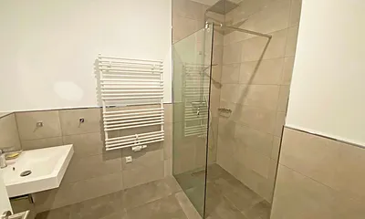 innenliegendes Bad mit einem Waschtisch, beheiztem und beleuchtetem Spiegel, Handtuchheizung, Fön, Kosmetikspiegel, WC sowie eine große ebenerdige Klarglas-Dusche mit Regenduschkopf