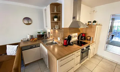 angrenzende Pantry-Küche mit Edelstahlspüle, 4-Zonen-Cerankochfeld, Kühlschrank mit Gefrierfach, Geschirrspüler, Mikrowelle, Dunstabzugs-Kombination, Kaffeemaschine, Wasserkocher und Toaster