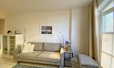 Wohnbereich mit bodentiefen Fenstern, 3-Sitzer-Couch, Couchtisch, Smart-TV, DVD-Player, Radio mit CD-Player und USB-Anschluss sowie eine Alexa-Box