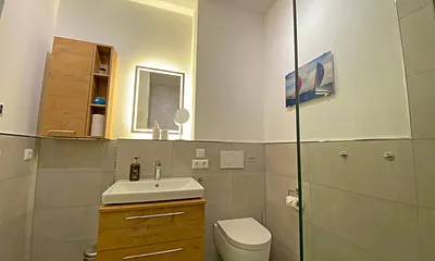 innenliegendes Badezimmer mit Waschtisch, Wandspiegel, ebenerdiger Regendusche, WC, Fön und Handtuchtrockner