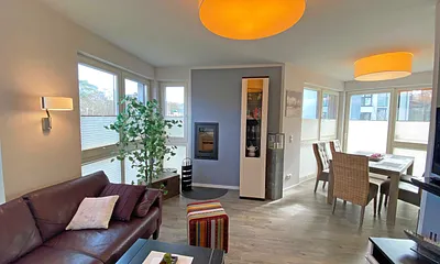 lichtdurchfluteter Wohnbereich mit Kamin, große Ledercouch, Couchtisch mit Hocker, Sideboard, Vitrine, Smart-TV mit Blu-Ray-Player sowie eine kleine Auswahl an Urlaubslektüre und CD`s