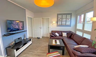 lichtdurchfluteter Wohnbereich mit Kamin, große Ledercouch, Couchtisch mit Hocker, Sideboard, Vitrine, Smart-TV mit Blu-Ray-Player sowie eine kleine Auswahl an Urlaubslektüre und CD`s