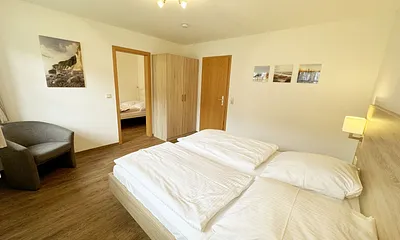 Schlafzimmer hell und modern eingerichtet mit Doppelbett, Komfortmatratzen (2x 0,90 m x 2,00 m), Nachttischkonsolen, Kleiderschrank und Verdunklungsgardinen