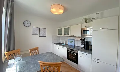 angrenzende Küchenzeile mit Geschirrspüler, Mikrowelle, Ceranfeld, Backofen, Kühlschrank mit Gefrierfach, Wasserkocher, Toaster, Kaffeemaschine und diverse Küchenutensilien