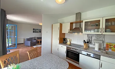 angrenzende Küchenzeile mit Geschirrspüler, Mikrowelle, Ceranfeld, Backofen, Kühlschrank mit Gefrierfach, Wasserkocher, Toaster, Kaffeemaschine und diversen Küchenutensilien 