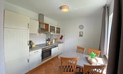 angrenzende Küchenzeile mit Geschirrspüler, Mikrowelle, Ceranfeld, Backofen, Kühlschrank mit Gefrierfach, Wasserkocher, Toaster, Kaffeemaschine und diversen Küchenutensilien 