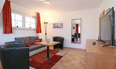 Wohnzimmer mit Schlafcouch (Aufbettung für 5./6. Person 1,37 m x 1,97 m), Stehlampe, zwei Sessel, Smart-TV sowie ein CD und Blu-Ray-Player