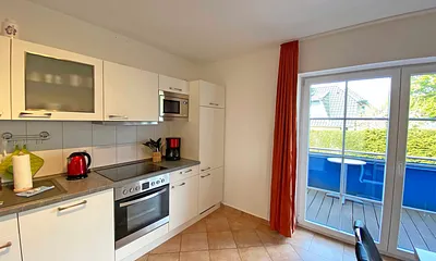 angrenzende Küchenzeile mit Geschirrspüler, Mikrowelle, 4 Zonen-Ceranfeld, Backofen, Kühlschrank mit Gefrierfach, Wasserkocher, Toaster, Kaffeemaschine und diversen Küchenutensilien 