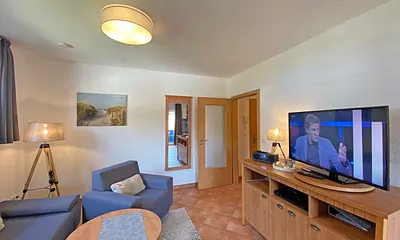 Wohnbereich mit Massivmöbeln, Stehlampe, zwei Sessel, Couch, LCD-TV und ein CD/ DVD-Player