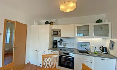 angrenzende Küchenzeile mit Geschirrspüler, Mikrowelle, Ceranfeld, Backofen, Kühlschrank mit Gefrierfach, Wasserkocher, Toaster, Kaffeemaschine und diverse Küchenutensilien