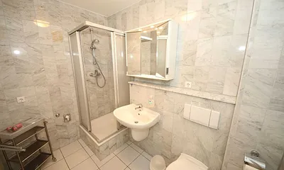 Badezimmer mit Marmorfliesen, Dusche, Kosmetikspiegel, Waschtisch, Fön und WC