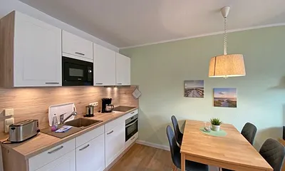 offene Küchenzeile mit Ceranfeld, Kompaktbackofen, Geschirrspüler, Mikrowelle, Spüle, Kühlschrank mit Gefrierfach und diverse Elektrokleingeräte und Küchenutensilien