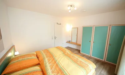 Schlafzimmer mit Doppelbett (1,80 m x 2,00 m), Schrank, Ablageflächen und bodentiefe Fenster mit Verdunklungsvorhängen