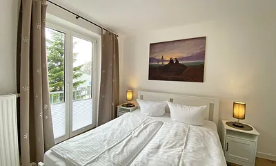 Schlafzimmer mit Doppelbett (1,60 m x 2,00 m, H3), Nachttischablagen, Kleiderschrank, Kommode, Smart-TV sowie Verdunklungsvorhang