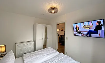 Schlafzimmer mit Doppelbett (1,60 m x 2,00 m, H3), Nachttischablagen, Kleiderschrank, Kommode, Smart-TV sowie Verdunklungsvorhang