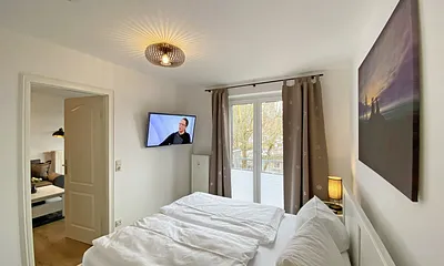 Schlafzimmer mit Doppelbett (1,60 m x 2,00 m, H3), Nachttischablagen, Kleiderschrank, Kommode, Smart-TV sowie Verdunklungsvorhang