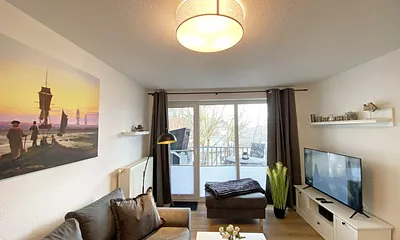 Wohnbereich mit gemütlicher Couch mit Ottomane, Couchtisch, Leselampe, kleines Highboard sowie TV-Board mit Smart-TV und DAB-Radio mit Bluetooth, USB und AUX