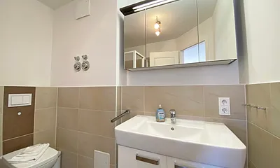 Badezimmer mit ebenerdiger Dusche, Waschtisch, WC, Handtuchtrockner und Fön