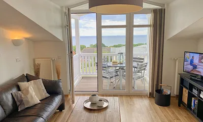 Wohnbereich mit bequemer Ledercouch, Lesesessel mit Hocker, Couchtisch, TV-Board mit Flachbild-TV, Musikanlage und Urlaubslektüre 