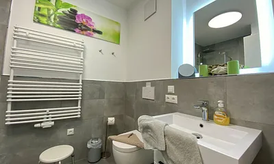 Badezimmer mit ebenerdiger Dusche, Waschtisch mit Spiegel, Handtuchheizkörper, Fön, Kosmetikspiegel, WC und Waschmaschine