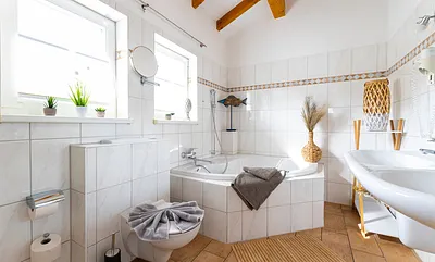 Badezimmer mit geräumiger Eck-Badewanne, WC, Fön, Kosmetikspiegel und ein Doppelwaschplatz mit dazugehörigem Spiegel