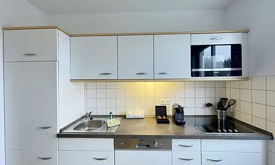 moderne Einbauküche mit Induktionsherd, Kühlschrank mit Gefrierfach, Mikrowelle, Geschirrspüler, Filter-Kaffeemaschine, Nespresso-Kapselmaschine, Wasserkocher, Toaster und Messerblock 