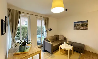 Wohnzimmer mit bequemer Eckcouch, Couchtisch, Stehlampe, 32-Zoll-Smart-TV, Bluetooth-Radio, Sideboard sowie eine Spielesammlung und kleine Auswahl an Büchern