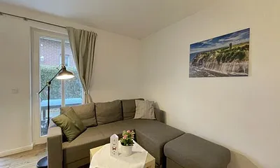 Wohnzimmer mit bequemer Eckcouch, Couchtisch, Stehlampe, 32-Zoll-Smart-TV, Bluetooth-Radio, Sideboard sowie eine Spielesammlung und kleine Auswahl an Büchern