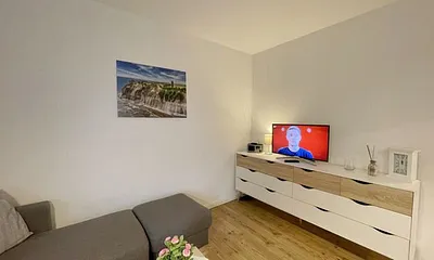 Wohnzimmer mit bequemer Eckcouch, Couchtisch, Stehlampe, 32-Zoll-Smart-TV, Bluetooth-Radio, Sideboard sowie eine Spielesammlung und kleine Auswahl an Büchern